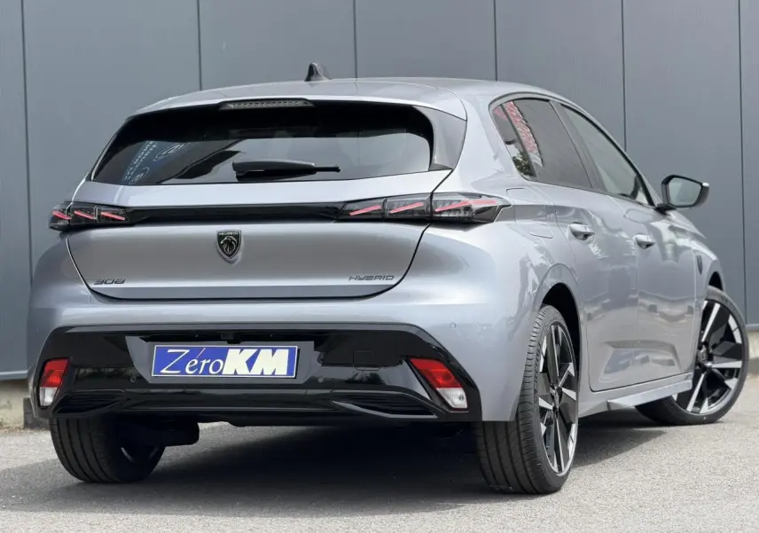 Vue 3/4 arrière droite d'une Peugeot 308 NV Hybrid 145 GT gris Artense avec jantes alliage bi-tons et feux arrière LED 3 griffes.