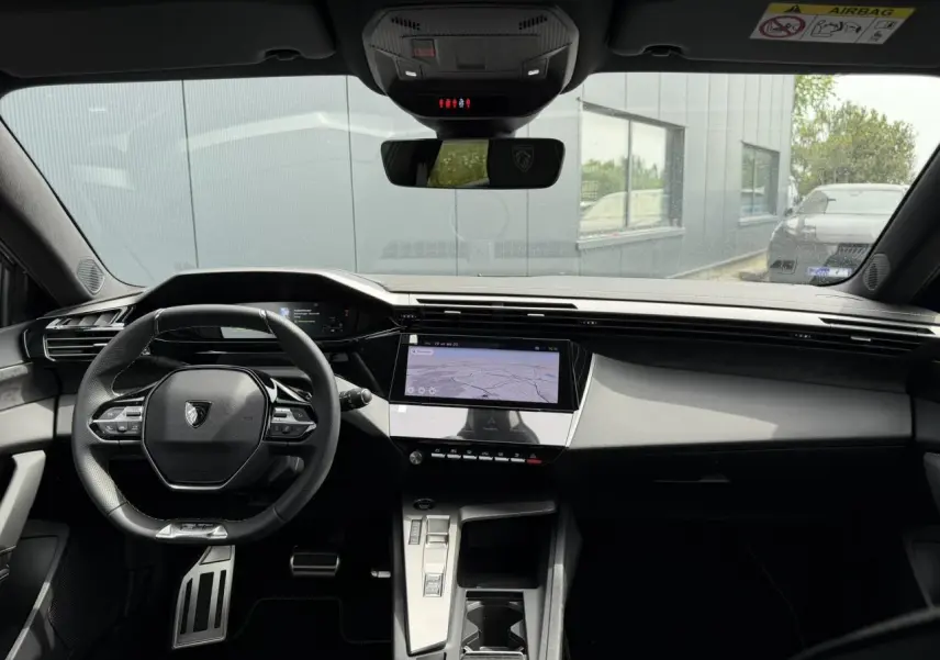 Vue intérieure avant du Peugeot 308 gris Artense, mettant en valeur le volant compact GT, l'écran tactile central et le combiné numérique.