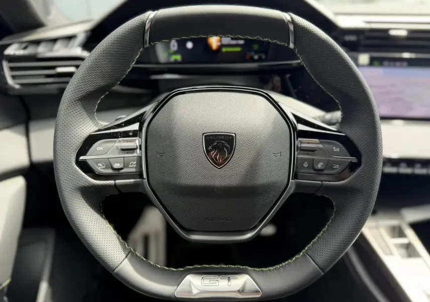 Volant compact GT en cuir noir avec surpiqûres vert Adamite et logo Peugeot, vue frontale centrée sur le volant.