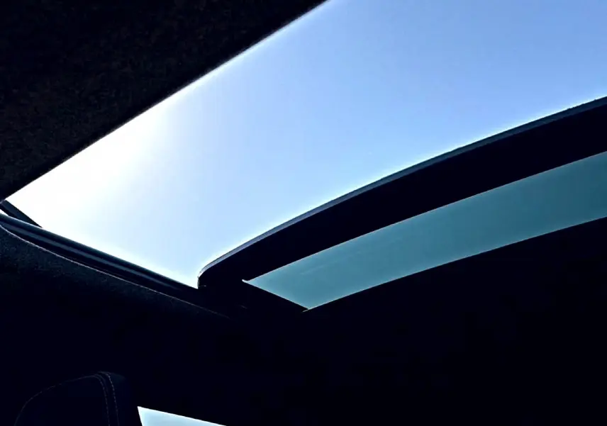 Toit panoramique en verre ouvert du Dacia Bigster blanc, vue intérieure vers le ciel bleu.