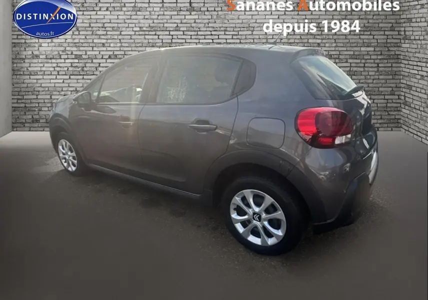 Citroën C3 gris foncé vue de profil côté gauche, stationnée devant un mur en briques grises.