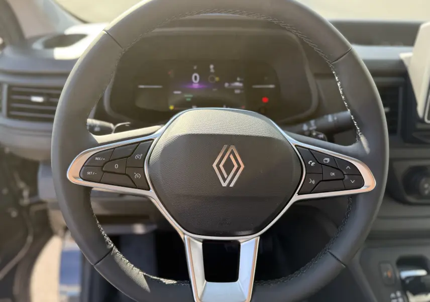 Vue rapprochée du volant noir du Renault Trafic L2H1 2025, avec commandes intégrées et logo central argenté.