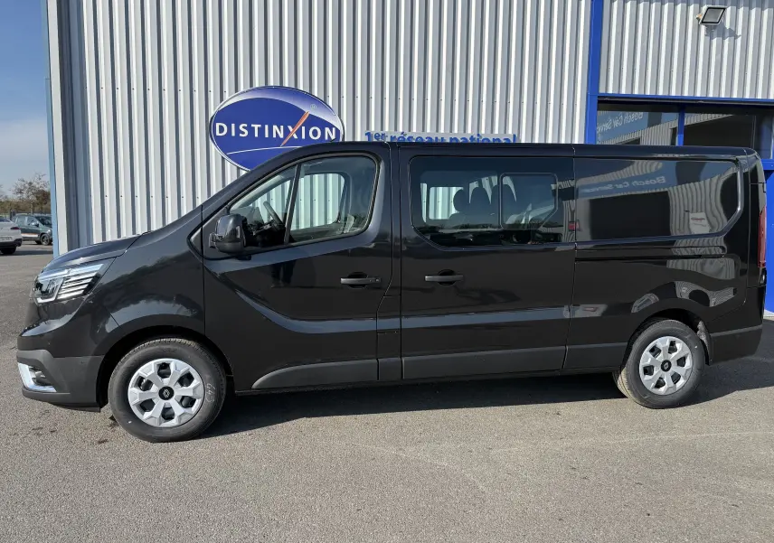 Profil côté gauche d’un Renault Trafic Cabine Approfondie noir 2025, stationné devant un bâtiment commercial.