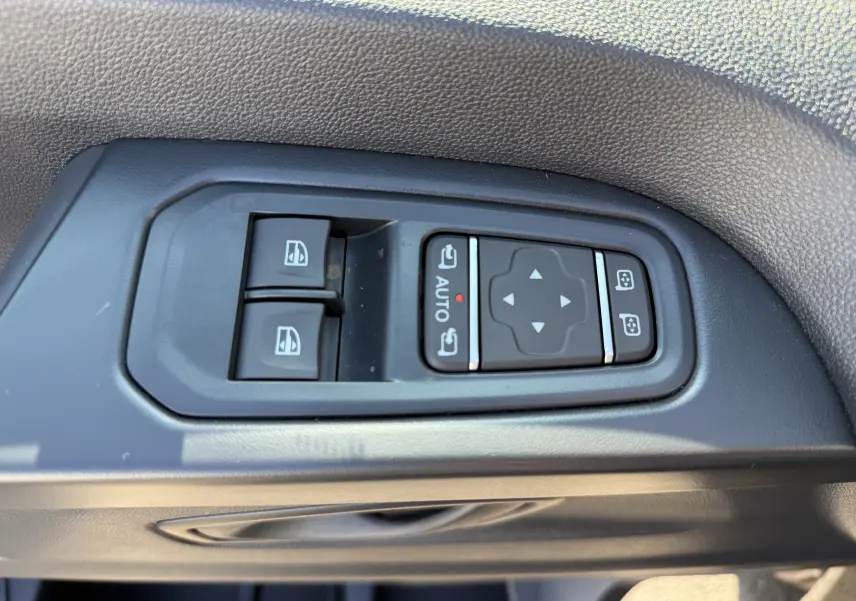 Gros plan sur les commandes de lève-vitres et réglage des rétroviseurs côté conducteur du Renault Trafic noir.