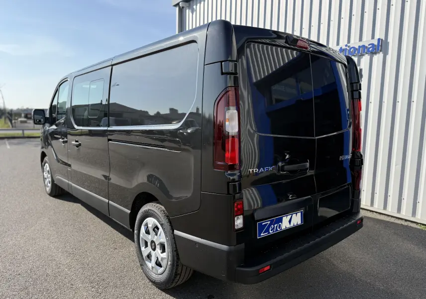Vue 3/4 arrière droite d’un Renault Trafic cabine approfondie noir 2025, avec vitres latérales teintées et feux arrière allongés.