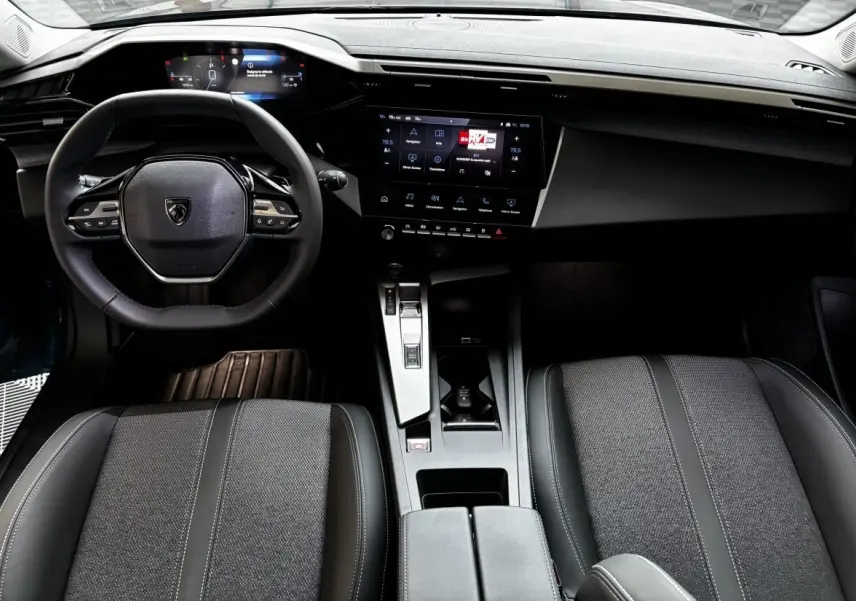 Vue intérieure avant de la Peugeot 308 Hybrid 136 e-DCS6 Allure 2025, volant cuir et écran tactile central noir.
