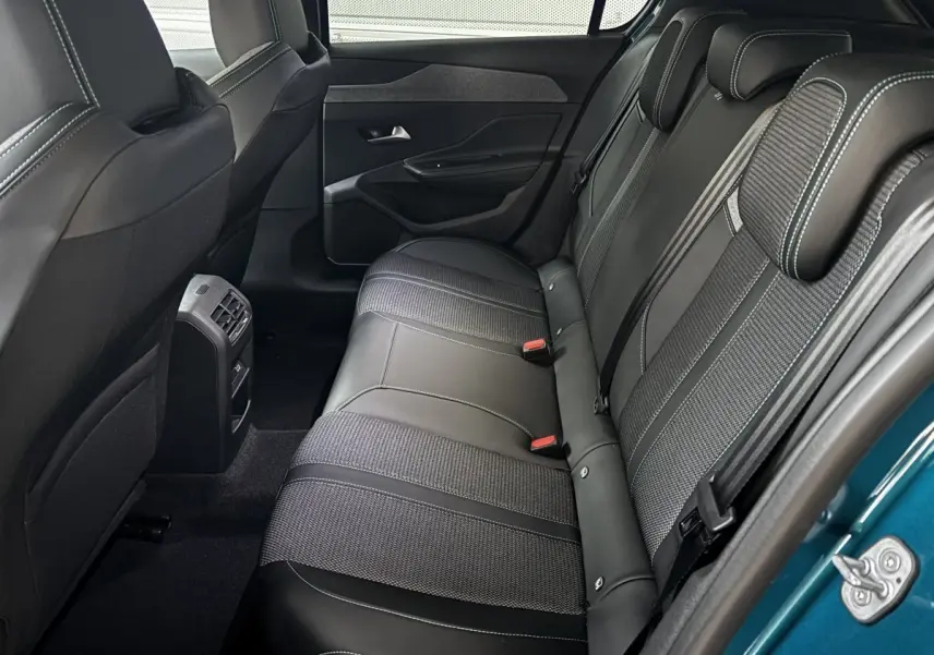 Vue intérieure côté arrière droit de la banquette en cuir noir et tissu de la Peugeot 308 Hybrid 2025 bleu visible à l'ouverture de porte.