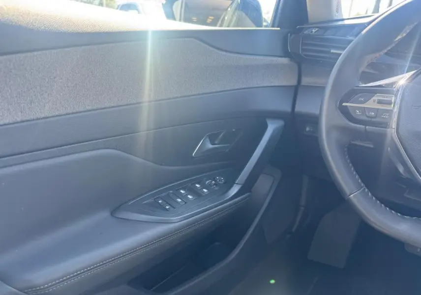 Intérieur côté conducteur d’une Peugeot 308 Hybrid gris, avec porte et commandes électriques, volant partiel et lumière naturelle.