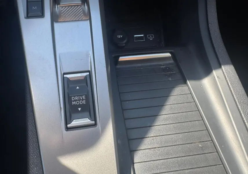 Gros plan sur la console centrale grise de la Peugeot 308 Hybrid 136 e-DCS6 Allure avec bouton Drive Mode et prise USB visible.