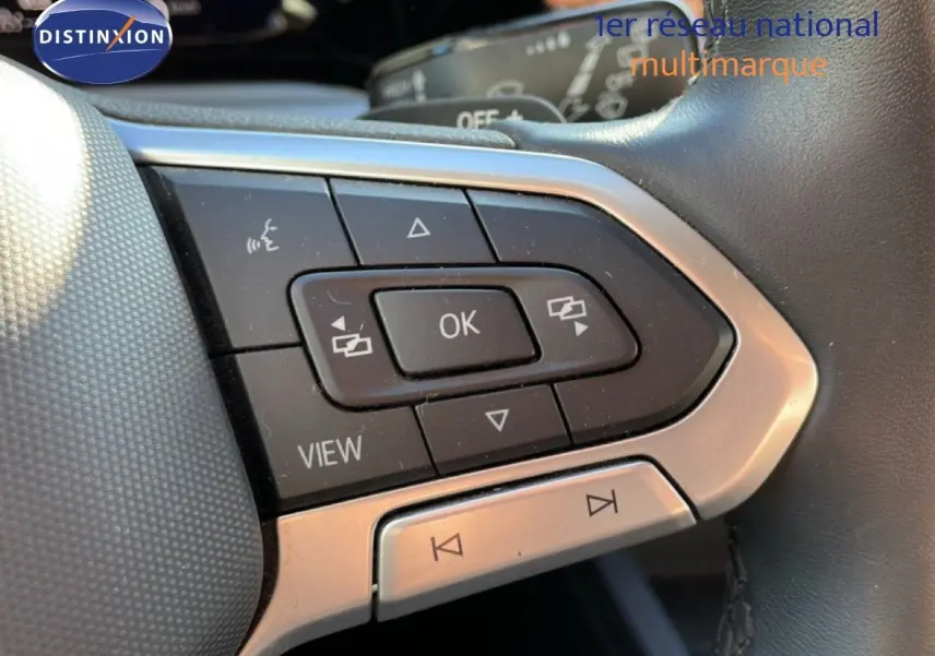 Gros plan sur les commandes multifonctions du volant noir de la Volkswagen Golf VIII rouge Roi Metal, touches OK et navigation visibles.