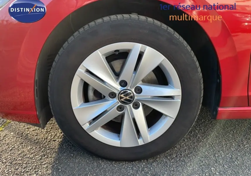 Gros plan sur la roue avant gauche d'une Volkswagen Golf VIII rouge Roi Metal avec jante alliage argentée.