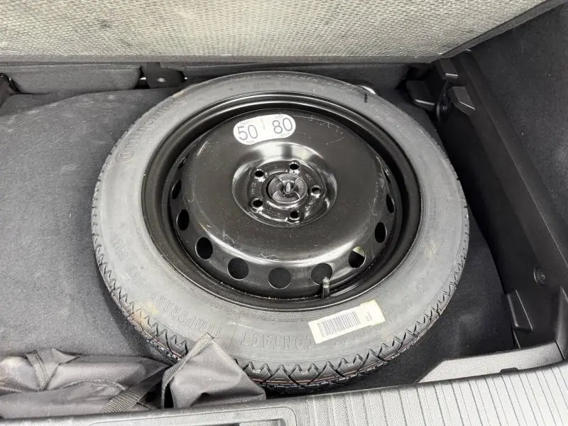 Roue de secours noire vue de dessus dans le coffre d’un Renault Captur 2025 Rouge Flamme hybride.