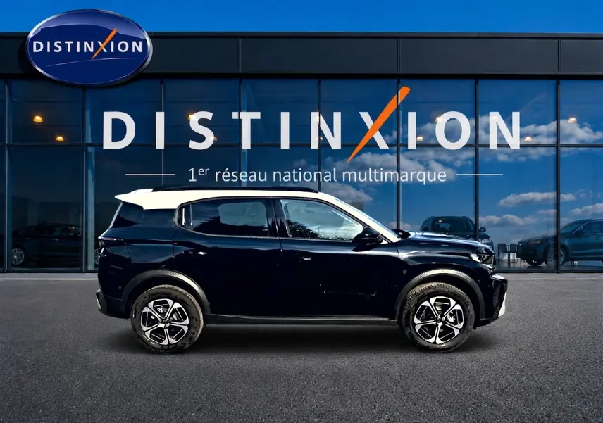 Profil côté gauche d'un Citroën C3 Aircross noir avec toit blanc, jantes alu distinctives, devant une vitrine Distinxion.