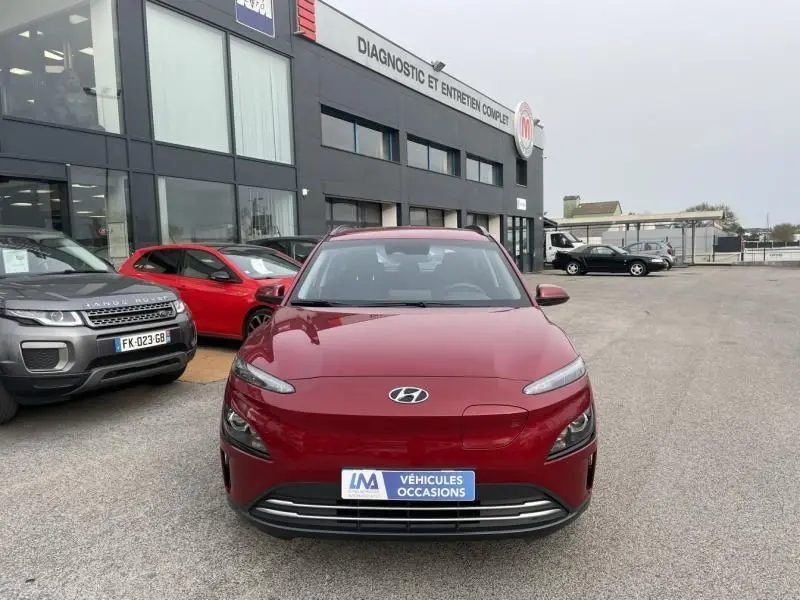 Vue de face d'un Hyundai Kona électrique rouge métal 2021 garé devant un centre de diagnostic automobile.