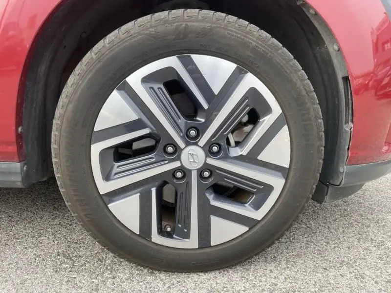 Gros plan sur la roue avant gauche d'une Hyundai Kona électrique rouge métal, mettant en valeur la jante au design moderne bicolore.
