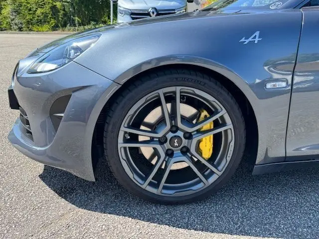 Gros plan sur la roue avant droite d'une Alpine A110 gris acier avec étrier de frein Brembo jaune et logo Alpine sur l'aile.