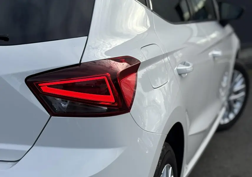 Gros plan sur le feu arrière gauche rouge d'une SEAT Ibiza blanche vue de trois quarts arrière côté gauche.