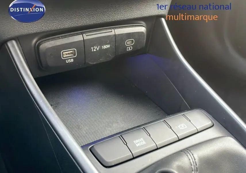 Gros plan sur la console centrale de la Hyundai i20 2025, montrant les ports USB, prise 12V et boutons de mode de conduite.
