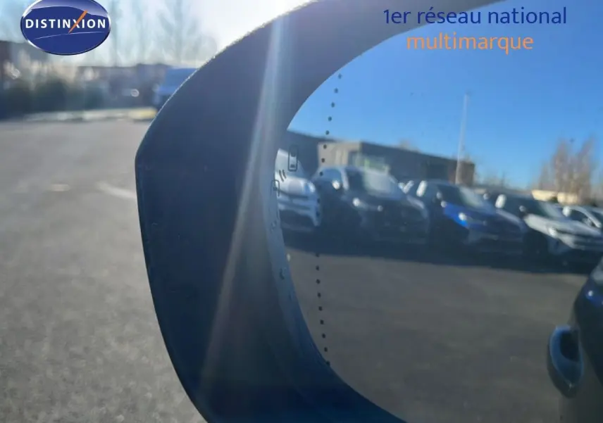 Rétroviseur gauche reflétant plusieurs voitures sur un parking par une journée ensoleillée.