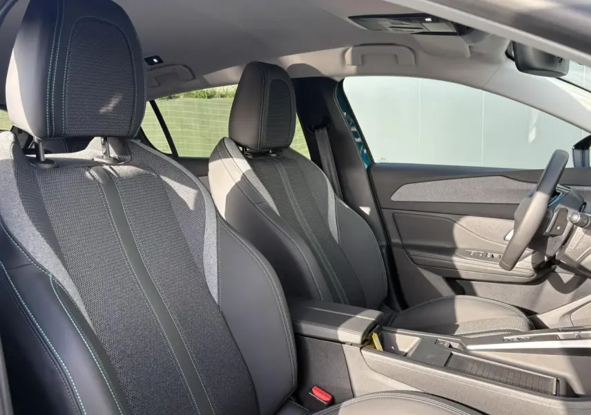 Vue intérieure côté conducteur de la Peugeot 308 Hybrid 145 Allure avec sièges tissu et cuir noirs et surpiqûres bleues.