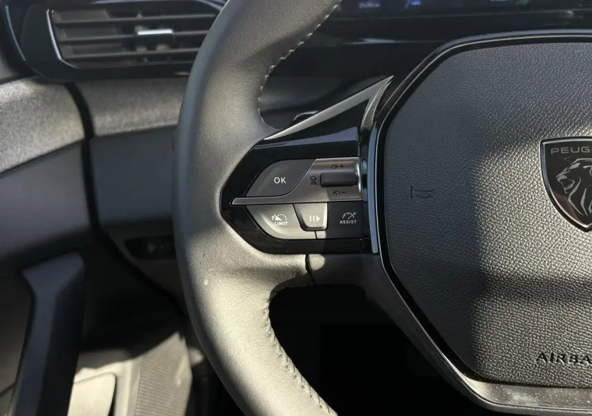 Gros plan sur le volant cuir noir de la Peugeot 308 Hybrid 2025, avec commandes intégrées et logo lion central.