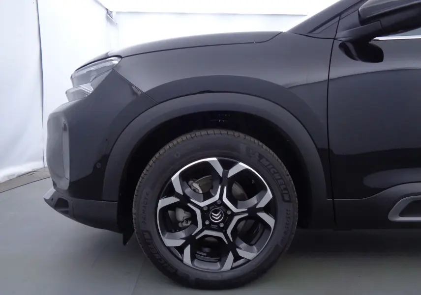 Gros plan sur la roue avant gauche du Citroën C5 Aircross noir métal, mettant en valeur la jante biton et le logo Citroën.