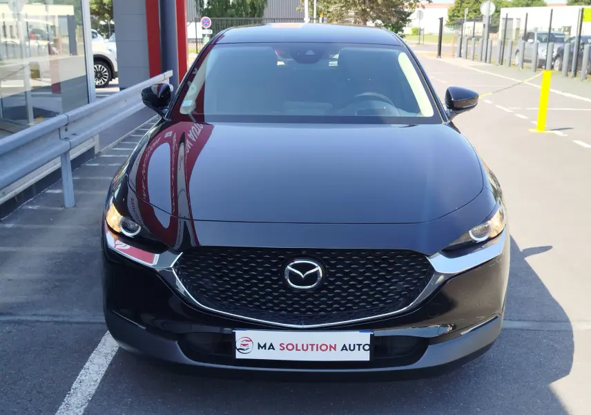 Vue frontale d'un Mazda CX-30 noir 2020 avec calandre noire et phares LED allumés en extérieur.
