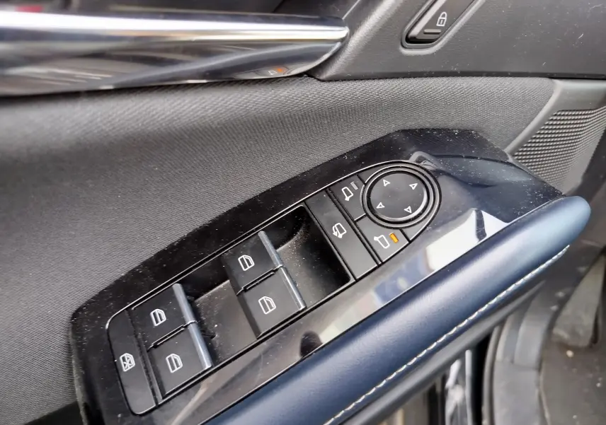 Gros plan sur les commandes des vitres et rétroviseurs côté conducteur du Mazda CX-30 noir, avec accoudoir en cuir bleu.