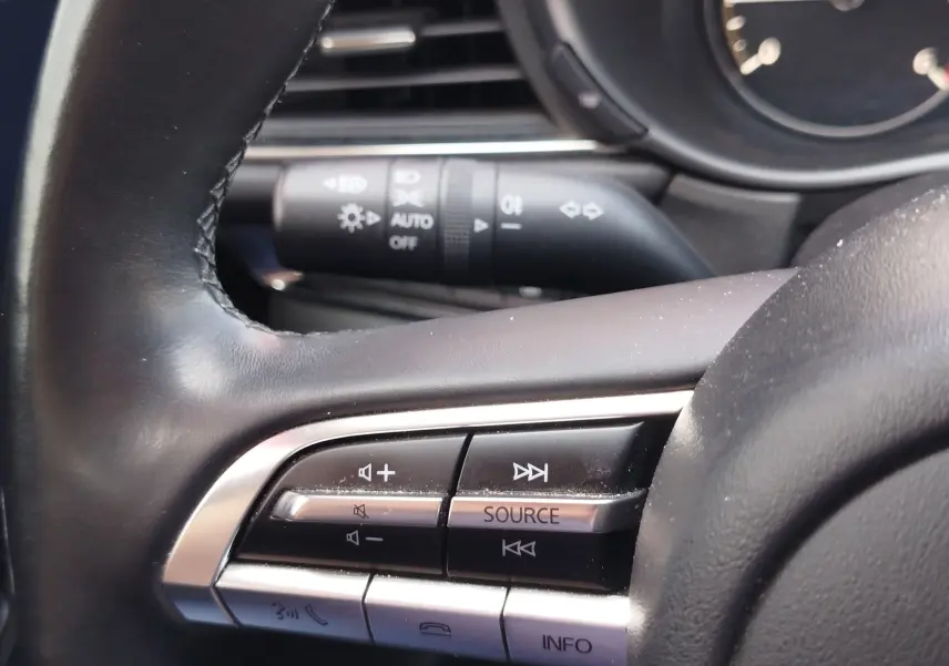 Gros plan sur les commandes audio au volant d'un Mazda CX-30 noir, avec boutons de volume et source sonore visibles.
