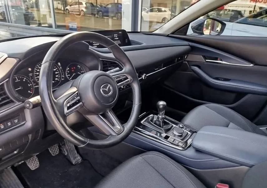 Vue intérieure côté conducteur du Mazda CX-30 2020 noir, avec volant multifonction et levier de vitesses manuel.