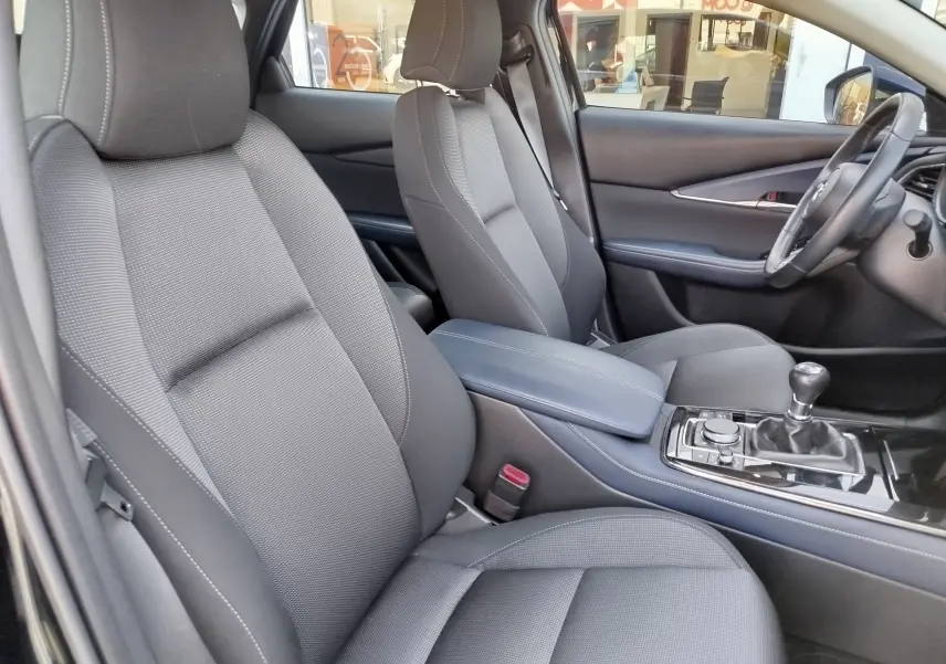 Vue intérieure côté conducteur du Mazda CX-30 noir 2020, sièges tissu noir et levier de vitesses manuel visible.