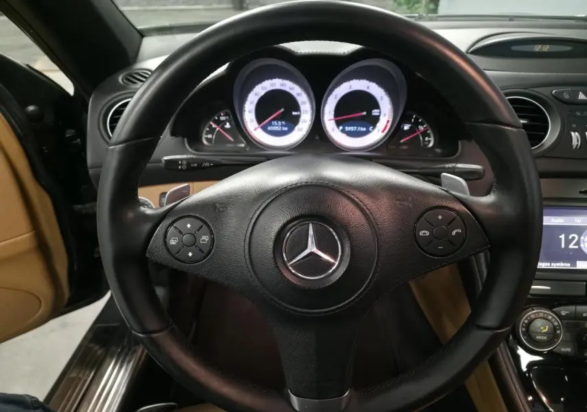 Vue rapprochée du volant cuir noir multifonctions d'une Mercedes SL 500 de 2008 avec tableau de bord éclairé.