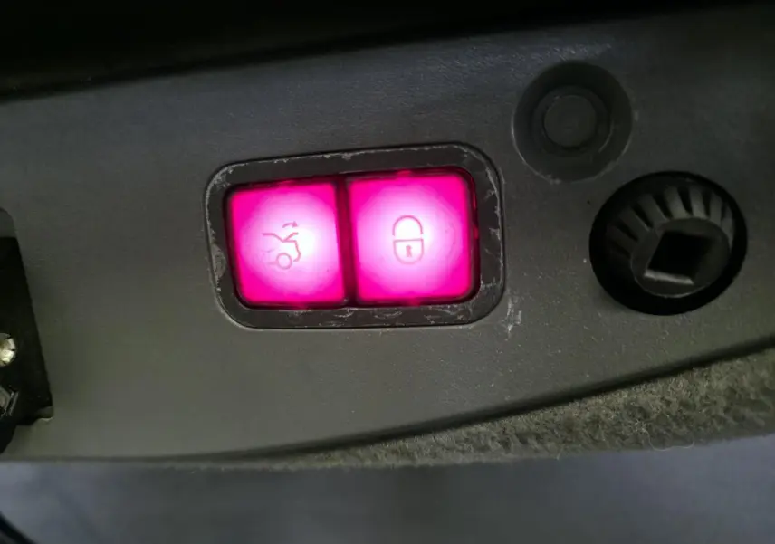 Gros plan sur les boutons lumineux roses de fermeture électrique du coffre et de verrouillage dans le coffre d'une Mercedes SL 500 noire.