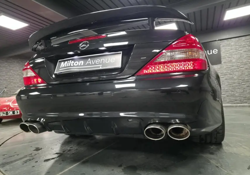 Vue arrière basse d'une Mercedes SL 500 noire avec double sortie d'échappement et aileron AMG en intérieur showroom.
