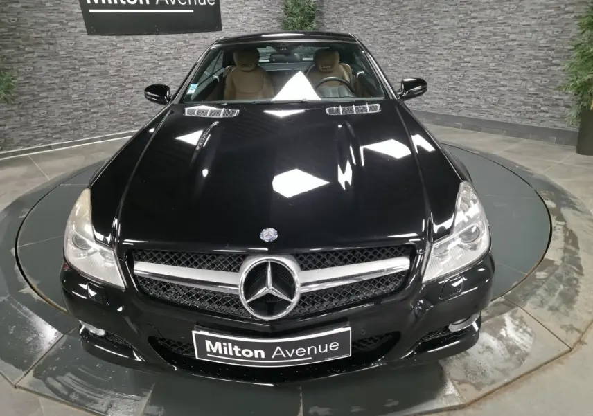 Vue avant plongeante d'une Mercedes SL 500 noire avec calandre AMG et intérieur cuir beige visible.