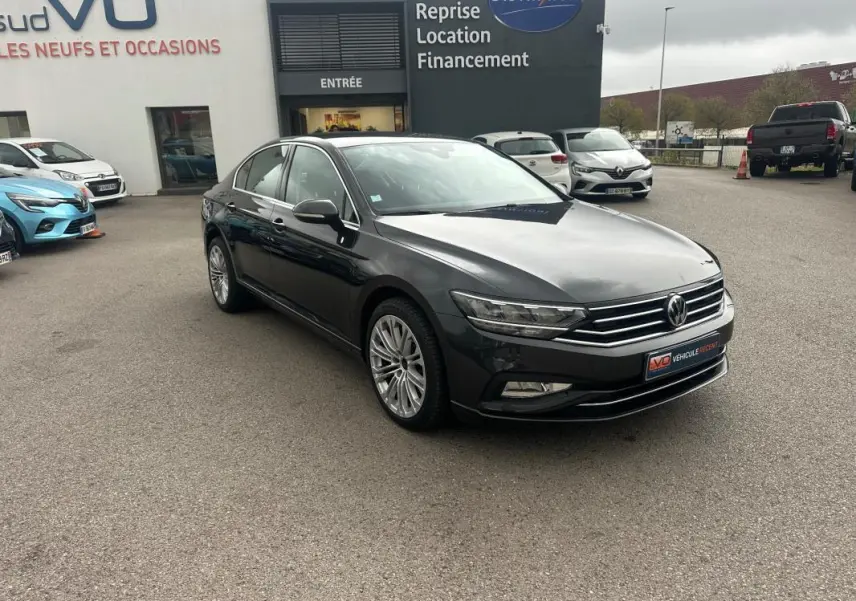 Volkswagen Passat gris foncé vue 3/4 avant droit sur parking devant concession automobile.