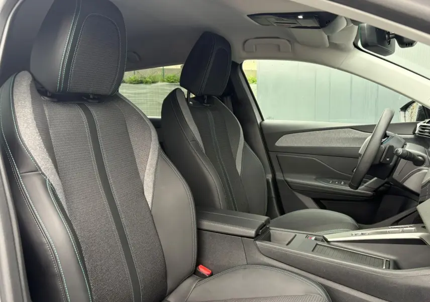 Vue intérieure côté conducteur de la Peugeot 308 SW Hybrid 145, sièges tissu et cuir noir avec surpiqûres vertes.