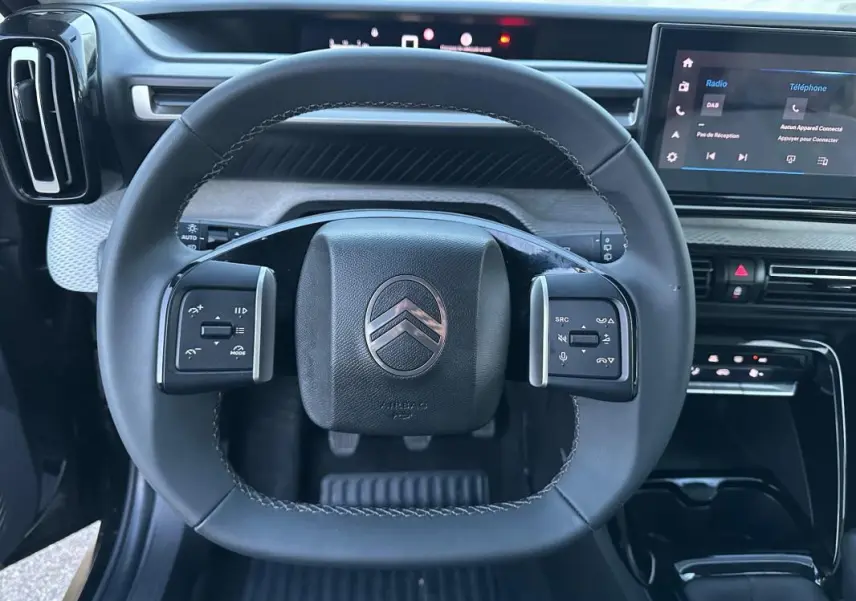 Vue intérieure centrée sur le volant noir de la Citroën C3 2025 avec commandes intégrées et écran tactile visible.