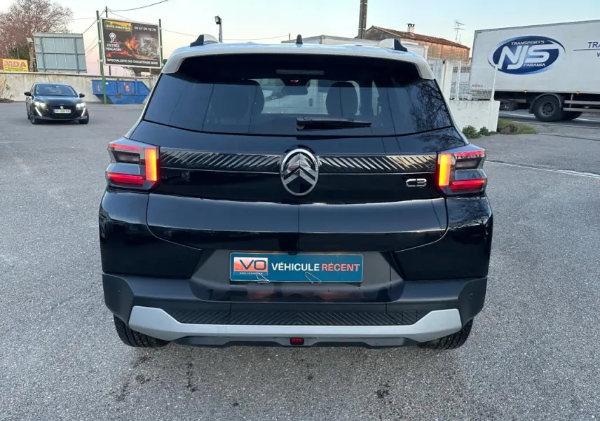 Vue arrière d'une Citroën C3 noire 2025 avec barres de toit et jantes alliage 17 pouces sur parking.