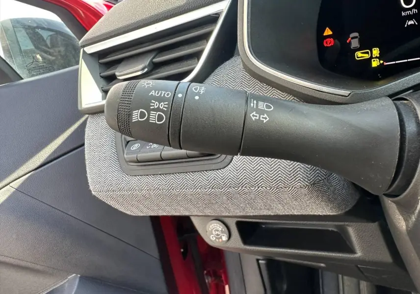 Gros plan sur la commande des phares à gauche du volant dans l’habitacle rouge flamme de la Renault Clio 2025.