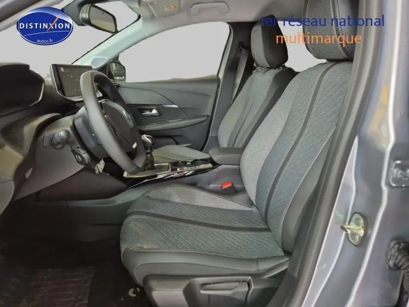 Vue intérieure côté conducteur de la Peugeot 208 1.2 100ch Allure 2025 avec sièges tissu gris et volant multifonction.