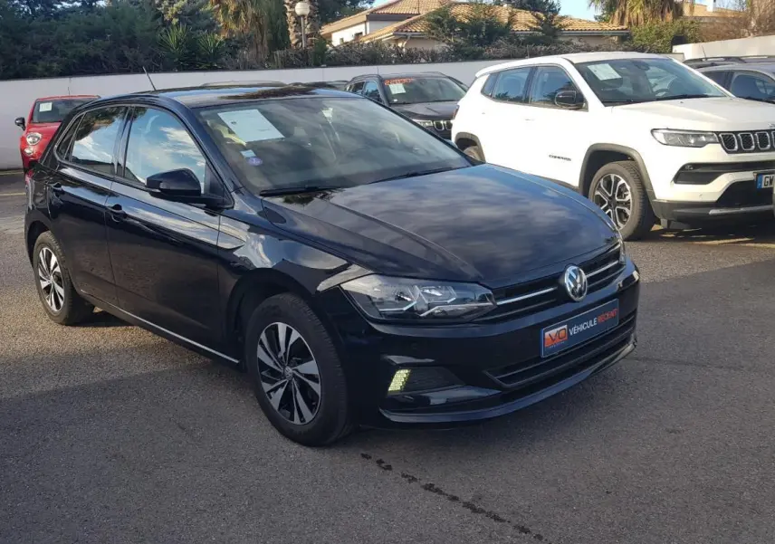 Volkswagen Polo noire vue en 3/4 avant droit avec jantes alliage et feux diurnes allumés sur parking.