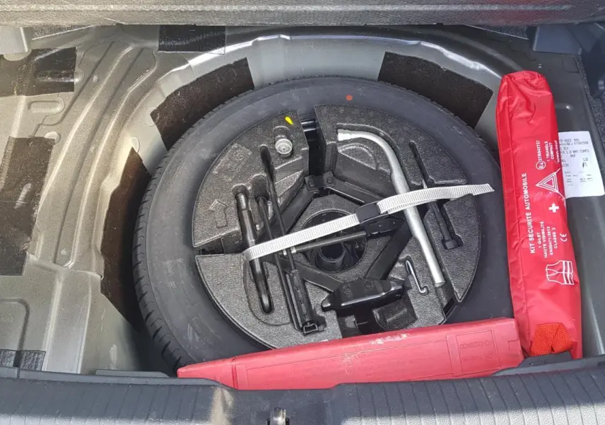 Gros plan sur la roue de secours et le kit de sécurité rouge dans le coffre d'une Volkswagen Polo noire de 2018.