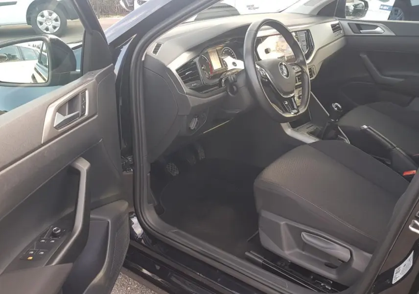 Intérieur côté conducteur d'une Volkswagen Polo noire 2018, volant multifonctions et siège réglable en hauteur visibles.