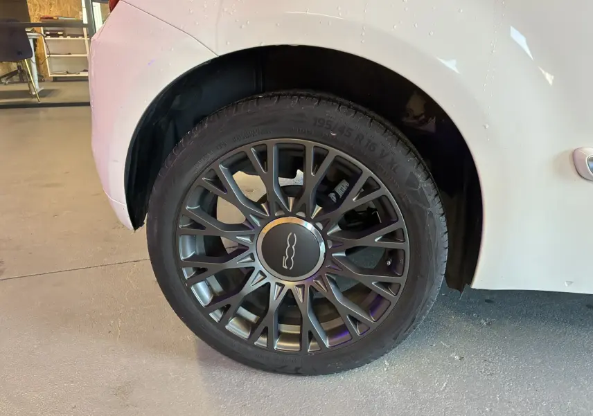 Gros plan sur la roue arrière droite d'une Fiat 500 blanche, mettant en valeur la jante alliage au design étoilé.