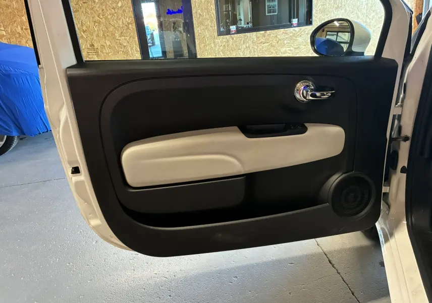 Vue intérieure de la porte avant gauche blanche d'une FIAT 500 2021, avec panneau noir et beige et poignée chromée.