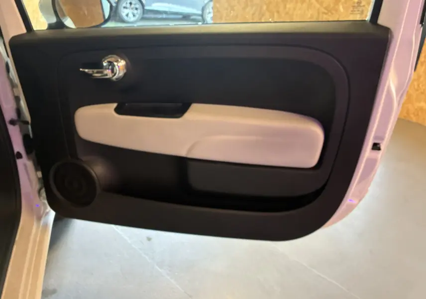 Vue intérieure de la porte côté gauche d'une Fiat 500 blanche, avec poignée chromée et panneau bicolore noir et beige.