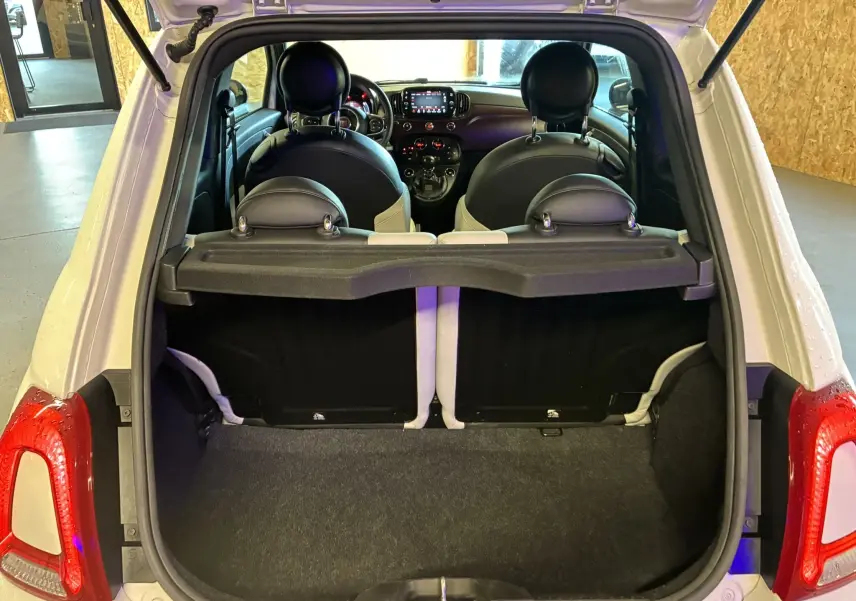 Vue arrière ouverte sur le coffre d'une Fiat 500 blanche, montrant l'intérieur avec sièges noirs et tableau de bord.