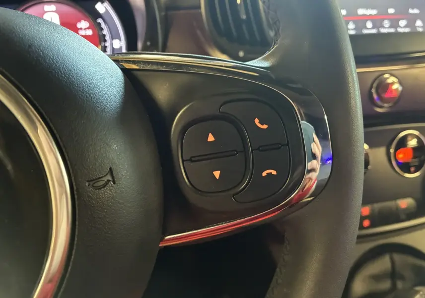 Gros plan sur les commandes du volant côté droit de la Fiat 500 blanche, avec tableau de bord et console en arrière-plan.