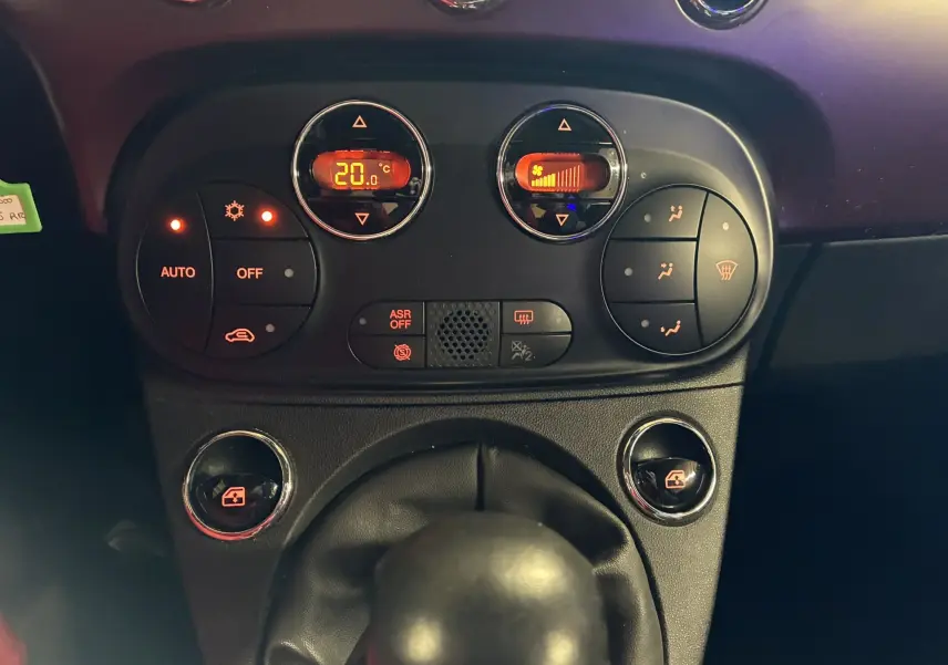 Gros plan sur la console centrale de la Fiat 500 blanche, montrant les commandes de climatisation et la boîte manuelle.